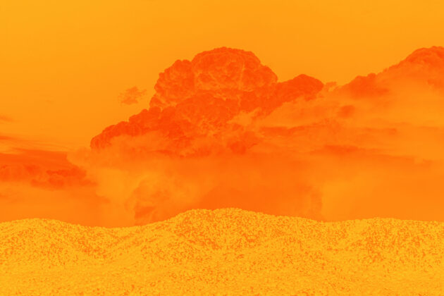 Deep dark orange clouds above the light hills of a desert landscape. The sky behind the cloud is orange and the entire canvas is bathed in orange.