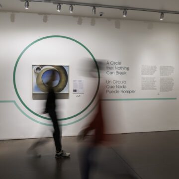 An exhibition with the blurry shapes of two people walking in front.