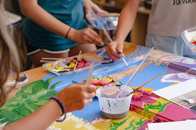 Photograph of young people's hands as they paint colorful flowers on a door.