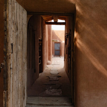 A doorway with an old wooden door opens up into an inner courtyard. The walls are made of adobe.