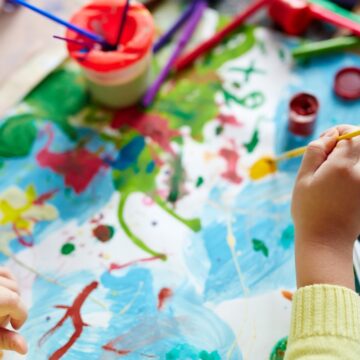 A child's hands pictured from above as they use colorful paints