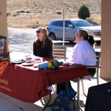 Two people sit at a table while another stand above.