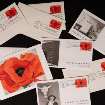 A collection of envelopes and cards with stamps featuring a huge orangish-red poppy with a black center stretches across the landscape-oriented composition. Its green stem is just visible at the bottom of the canvas. The flower contrasts with a plain white background.