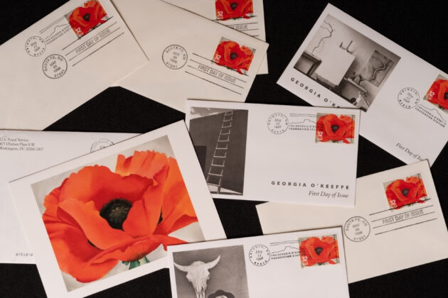 A collection of envelopes and cards with stamps featuring a huge orangish-red poppy with a black center stretches across the landscape-oriented composition. Its green stem is just visible at the bottom of the canvas. The flower contrasts with a plain white background.