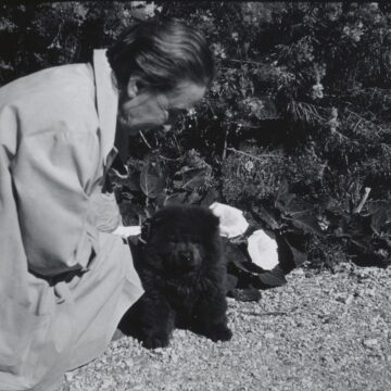 Black and white photograph of Georgia O'Keeffe kneeling down beside a small Chow Chow puppy.
