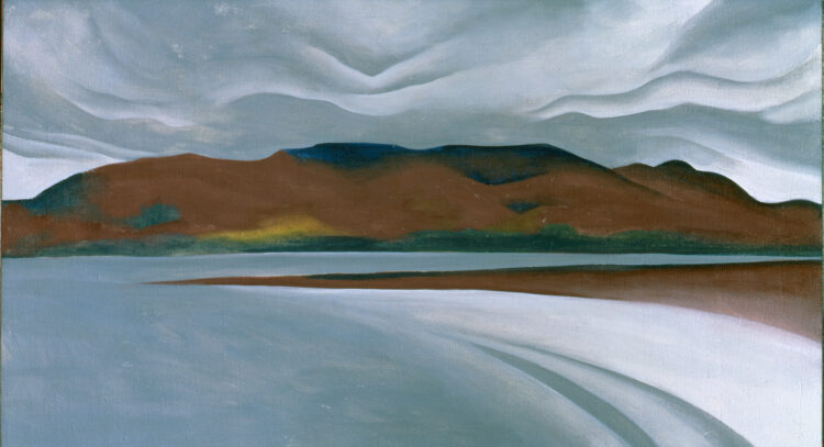 A lake with a white beach stretches across the foreground of the work. In the distance, brown and green mountains rise against a gray sky filled with rippling clouds.