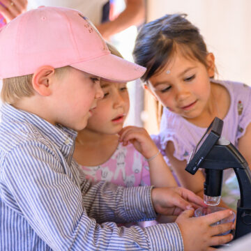 A group of three children look closely at a microscope.
