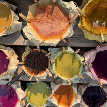 Several buckets filled with various natural pigments in shades of yellow, orange, purple, and pink.