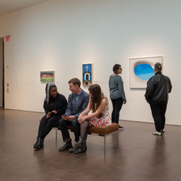 Three young adults sit at a bench and smile at each other. Georgia O'Keeffe's Pelvis IV is in the background.