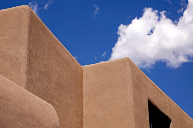 A corner of Georgia O'Keeffe Museum. The image is the top of the adobe colored walls and roof against a brilliant blue sky.
