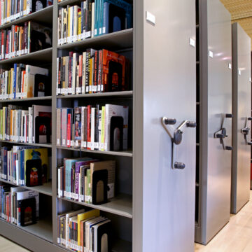 Shelves of books with library tags on them sitting in movable compact shelving with wheels to move them back and forth.